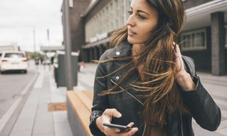 Young Woman With Windswept Hair Holding Cell Phone In The City